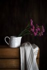 Frische lila Nelken im Becher auf dunklem Hintergrund mit Küchentuch — Stockfoto