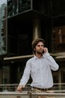 Портрет уверенного бизнесмена в белой рубашке, разговаривающего по смартфону и смотрящего в сторону на городскую сцену — стоковое фото