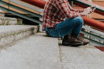 Кроп человек с помощью смартфона, сидя на ступеньках — стоковое фото