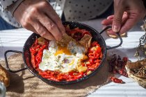 Close up view of hands holding pan with scrambled eggs and dried tomatoes on wooden table — Stock Photo