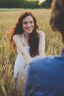 Portrait of happy red haired girl holding boyfriends hands in rye field — Stock Photo