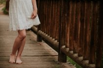 Нижняя часть девушки в белом платье ходит по деревянному мосту — стоковое фото