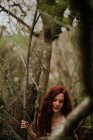 Serene gingembre fille en robe blanche marchant parmi les branches nues — Photo de stock