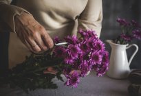 Close up view of female florist hands cutting with scissors purple flower petals — Stock Photo
