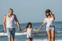 Retrato de la familia caminando por la playa y tomados de la mano . - foto de stock