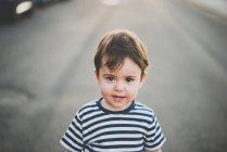 Портрет милого хлопчика в смугастих футболках дивиться на камеру на дорозі — стокове фото