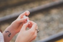 Visão de perto das mãos femininas enrolando cigarro sobre trilhos no fundo — Fotografia de Stock