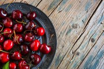 Fresh ripe cherries on black platter on wooden table — Stock Photo