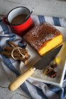 Vista de ángulo alto de la placa con pastel casero rural y cuchillo en la toalla con palos de canela y taza con chocolate caliente - foto de stock