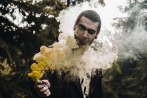 Porträt eines jungen Mannes, der eine Rauchkerze in der Hand im Wald betrachtet — Stockfoto