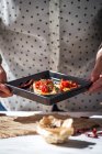 На кухонном столе средняя часть женщины держит сковороду с пенни-бастером, покрытым сушеными помидорами — стоковое фото
