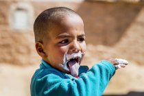 Хлопчик з кремом на обличчі показує язик — стокове фото