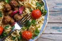 Above view of fork on plate full of pasta with meatballs and cherry tomatoes on rustic wooden table — Stock Photo