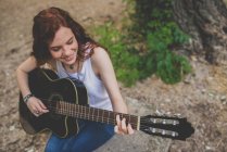Высокоугловой портрет улыбающейся веснушки, сидящей на роке и играющей на гитаре — стоковое фото
