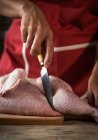 Крупным планом женщины режут сырую курицу на деревянной доске — стоковое фото