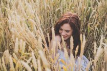 Retrato de alto ângulo de menina de cabelos vermelhos sorridente sentado em centeio e posando com os olhos fechados — Fotografia de Stock