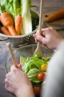 Over shoulder view of hands mixing salad in bowl — Stock Photo