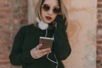 Chica sosteniendo teléfono inteligente y escuchar auriculares de música - foto de stock