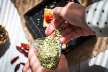 Above view of hand pouring herbs in palm over baking pan on kitchen table — Stock Photo