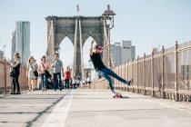 Молодой парень делает трюки и держит равновесие на скейтборде на мосту. — стоковое фото