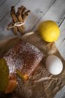 Высокий угол обзора ломтиков лимонного пирога на хлебобулочной бумаге с ингредиентами на деревенском белом деревянном столе — стоковое фото