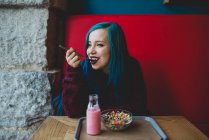 Портрет синьо волохатої дівчини, що їсть барвисті злаки за столом кафе — стокове фото