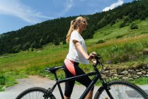 Chica caminando con bicicleta en el campo de montaña carretera - foto de stock