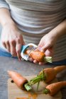 Manos de cultivo pelando zanahoria con pilar vegetal - foto de stock