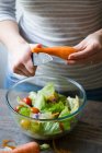 Mani di raccolto affettando la carota in ciotola d'insalata — Foto stock