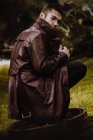 Retrato de homem de casaco de couro agachando no esgoto bueiro e olhando sobre o ombro para a câmera — Fotografia de Stock