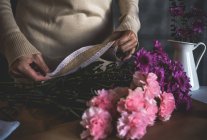 Mittelteil der Blumenhändlerin hält Schleife über Blumenstrauß auf Tisch — Stockfoto