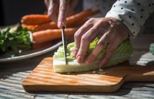 Close up view of hands slicing cabbage leaves on wooden board — Stock Photo