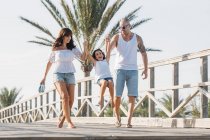 Family walking along bridge and pulling little girl up in air — Stock Photo