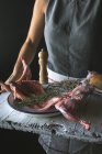 Крупним планом жінка тримає тушу сирого кролика з інгредієнтами на дерев'яному столі — стокове фото