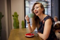 Молода весела жінка п'є каву в кав'ярні — стокове фото