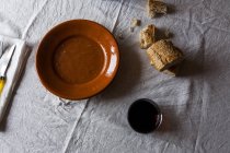Верхний вид стола с сельскими ломтиками хлеба, стаканом сока и сельской тарелкой на смятой белой скатерти — стоковое фото