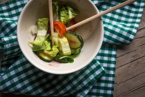 Частично съеденный свежий овощной салат в миске с палочками на ткани на деревянной поверхности — стоковое фото