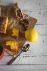 Natureza morta de partes de bolo de limão com temperos e limão em papel de padaria sobre a mesa de madeira rural — Fotografia de Stock