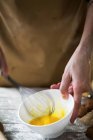 Vista da vicino mani femminili che sbattono le uova con la frusta nella ciotola di ceramica bianca — Foto stock