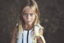 Fille manger banane et regarder caméra — Photo de stock