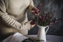 Mid section of female florist cutting with scissors flower in white ceramic vase on table — Stock Photo