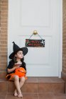 Girl in witch costume with pumpkin over open door — Stock Photo