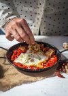 Vista da vicino di mano mettere ingrediente in padella con uova strapazzate e pomodori secchi — Foto stock