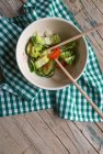 Parcialmente comido salada de legumes frescos em tigela com pauzinhos em tecido na superfície de madeira — Fotografia de Stock