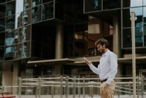 Side view of smiling businessman in white shirt using phone over business building facade at urban scene — Stock Photo