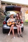 Mädchen sitzen mit Gitarre im Kofferraum — Stockfoto