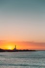 Meereslandschaft bei Sonnenuntergang mit Leuchtturm-Silhouette an der Küste — Stockfoto