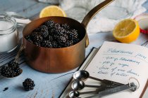 Blackberries in coper pot near notebook with recipe — Stock Photo