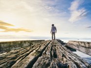 Back view of man standing on ruins of wooden pier on background of bright sky and sea. — Stock Photo