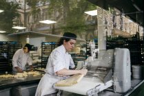 LONDRES, Reino Unido - 4 de mayo de 2017: Disparo a través de un vaso de una joven amasando pan con concentración en una panadería moderna  . - foto de stock